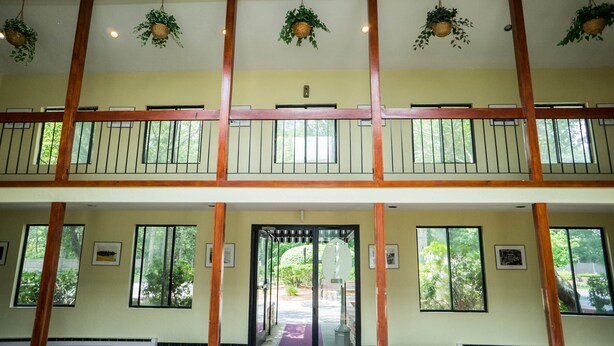 A two-story building with a balcony on the upper floor, large windows, and hanging plants.