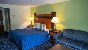 A hotel room with a bed, two bedside lamps, a nightstand, a sofa, and a wooden headboard.