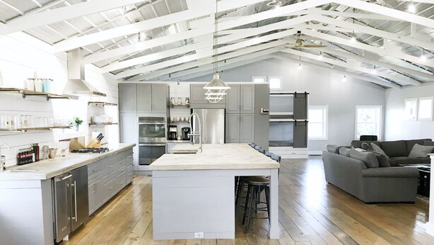 A spacious kitchen with a central island, modern appliances, and a high ceiling with exposed beams.