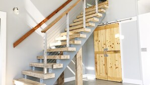 A modern staircase with wooden steps and metal railings, leading to a wooden door.