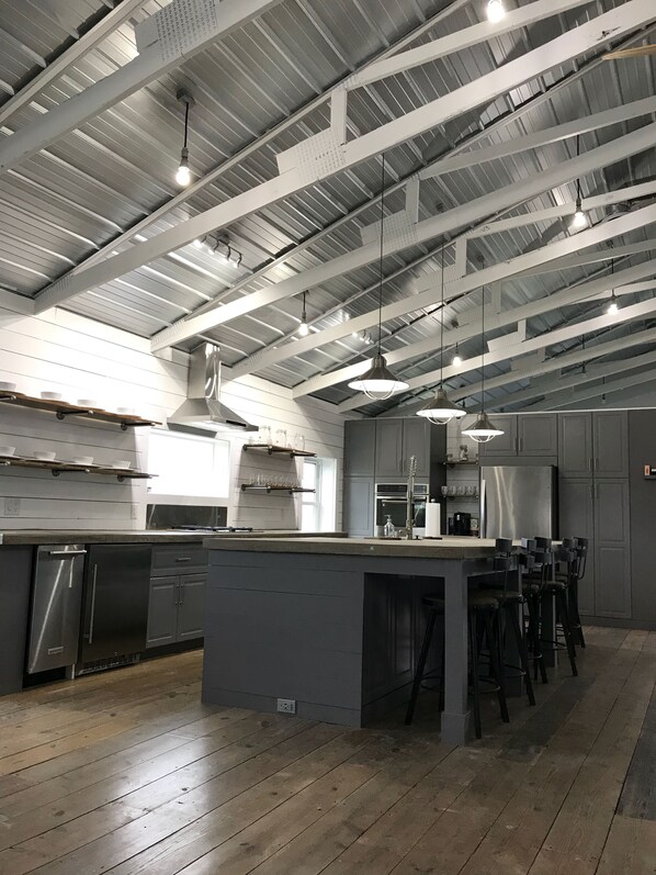 Una cocina moderna con electrodomésticos de acero inoxidable, una isla grande con taburetes de bar y un techo alto con vigas a la vista.