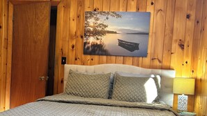 Ein Schlafzimmer mit Holzwänden, einem großen Bett, einem Bild von einem See und einem Nachttisch mit Lampe.