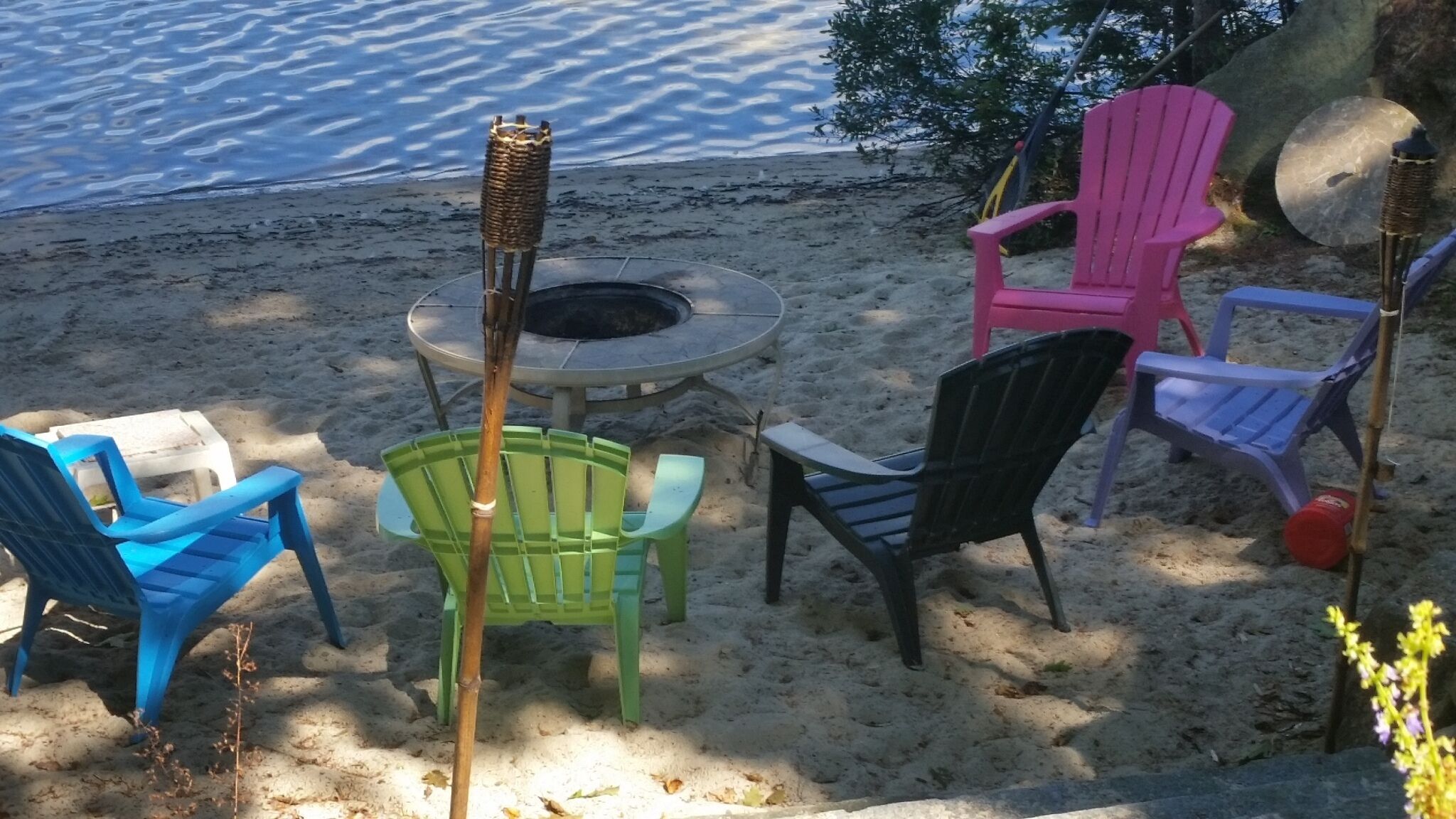 Un espace aménagé avec des sièges, situé au bord de la plage, comprenant un foyer et entouré de chaises en plastique de couleurs vives.