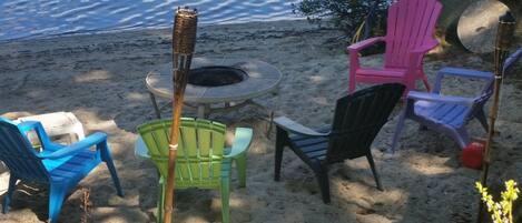 Un espace aménagé avec des sièges, situé au bord de la plage, comprenant un foyer et entouré de chaises en plastique de couleurs vives.