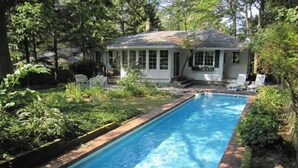 Une piscine rectangulaire bordée de briques, entourée d’une végétation luxuriante et d’arbres.