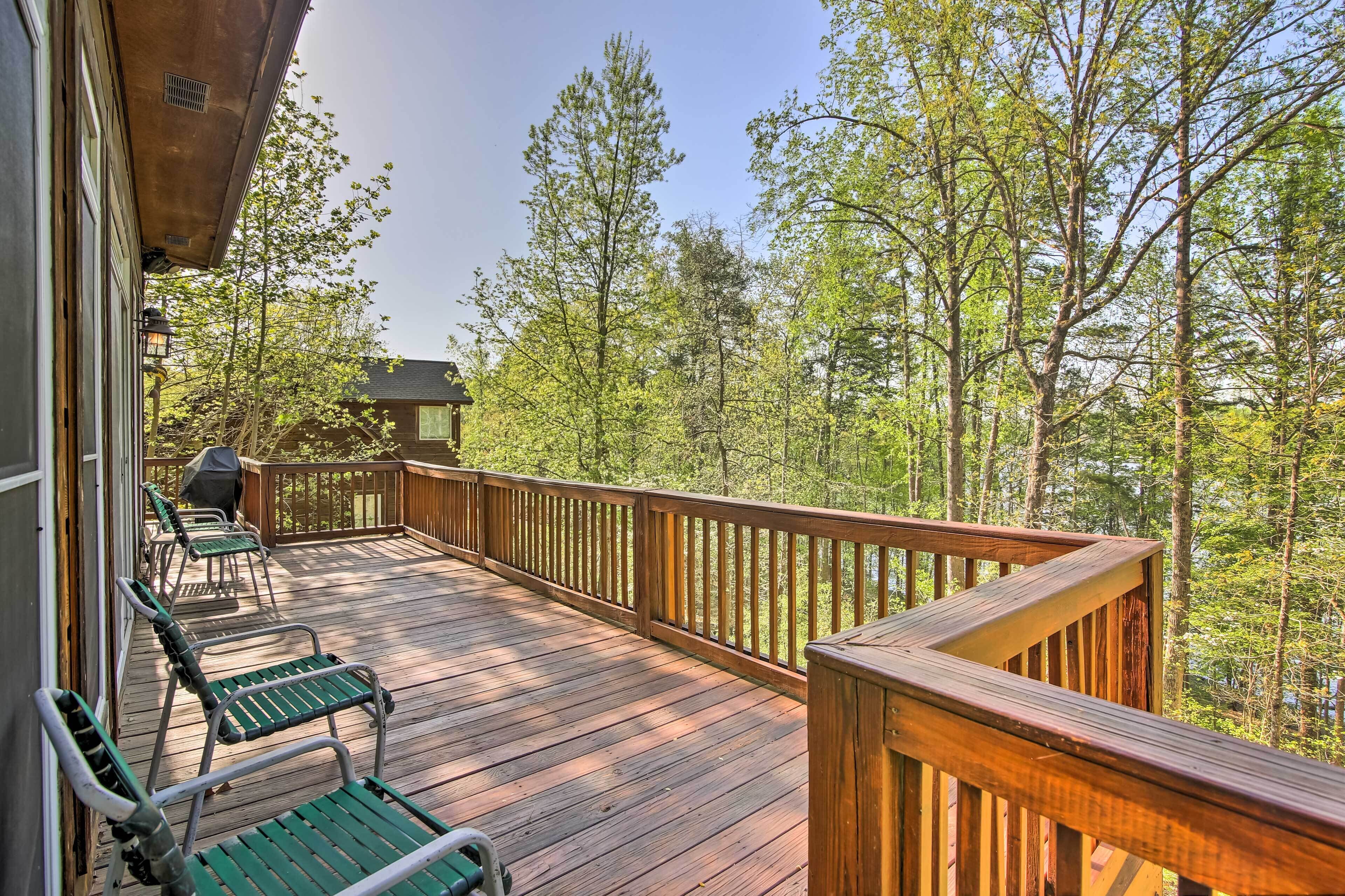 A wooden deck with green chairs, a grill, and a view of trees.