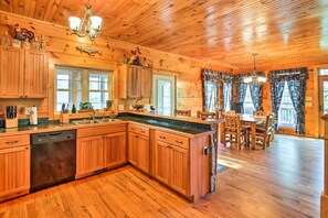 Interno di una baita in legno con cucina, caratterizzata da mobili in legno, lavastoviglie e zona pranzo con tavolo e sedie.