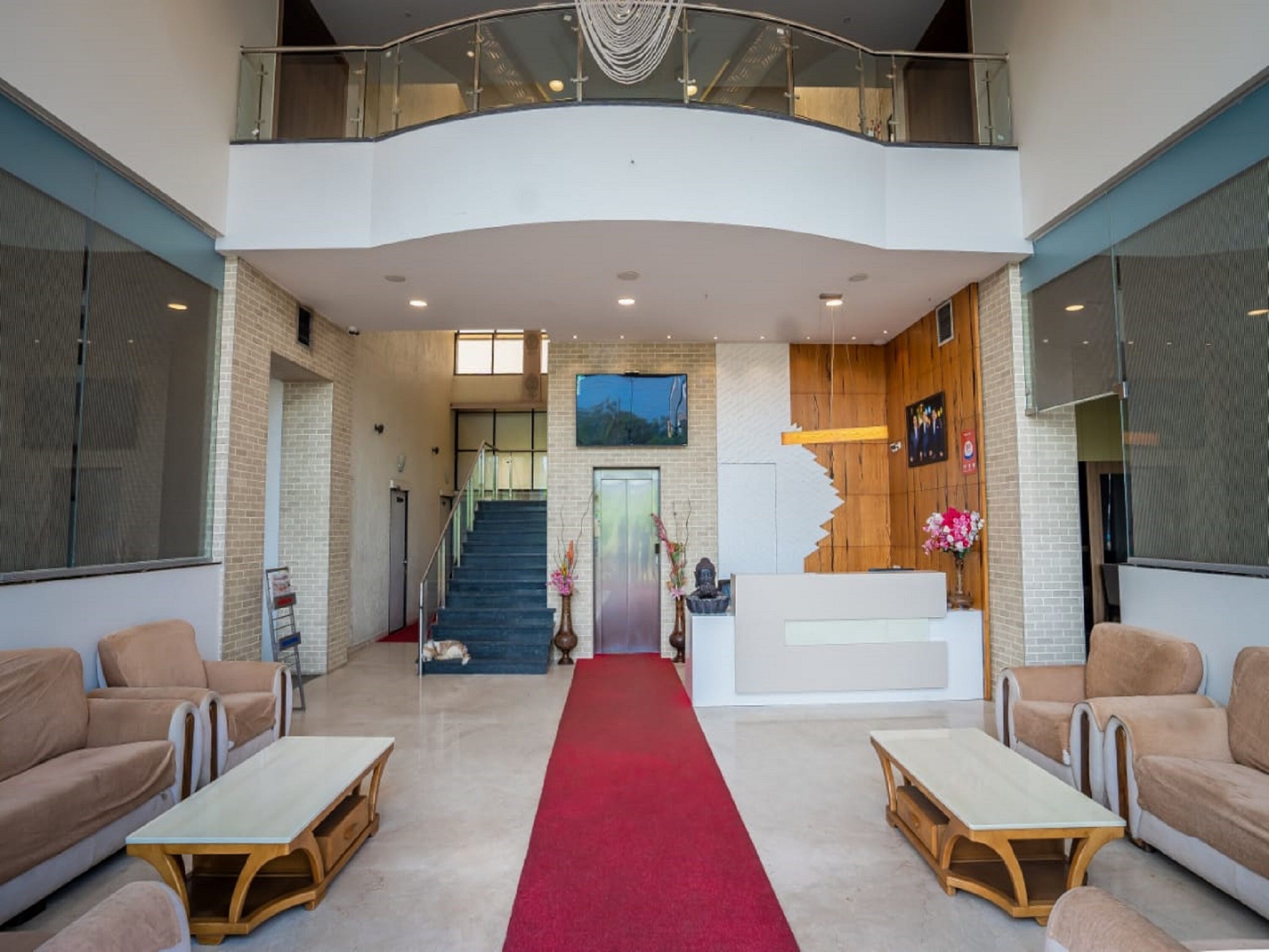 A spacious lobby with a red carpet, a reception desk, and a staircase leading to an upper level.