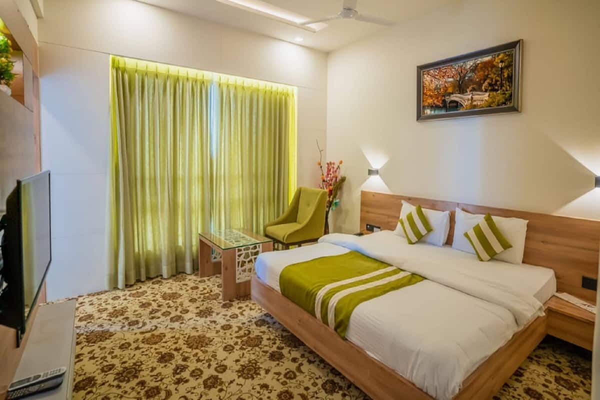 A hotel room with a bed, a chair, a desk, a television, and a painting on the wall.
