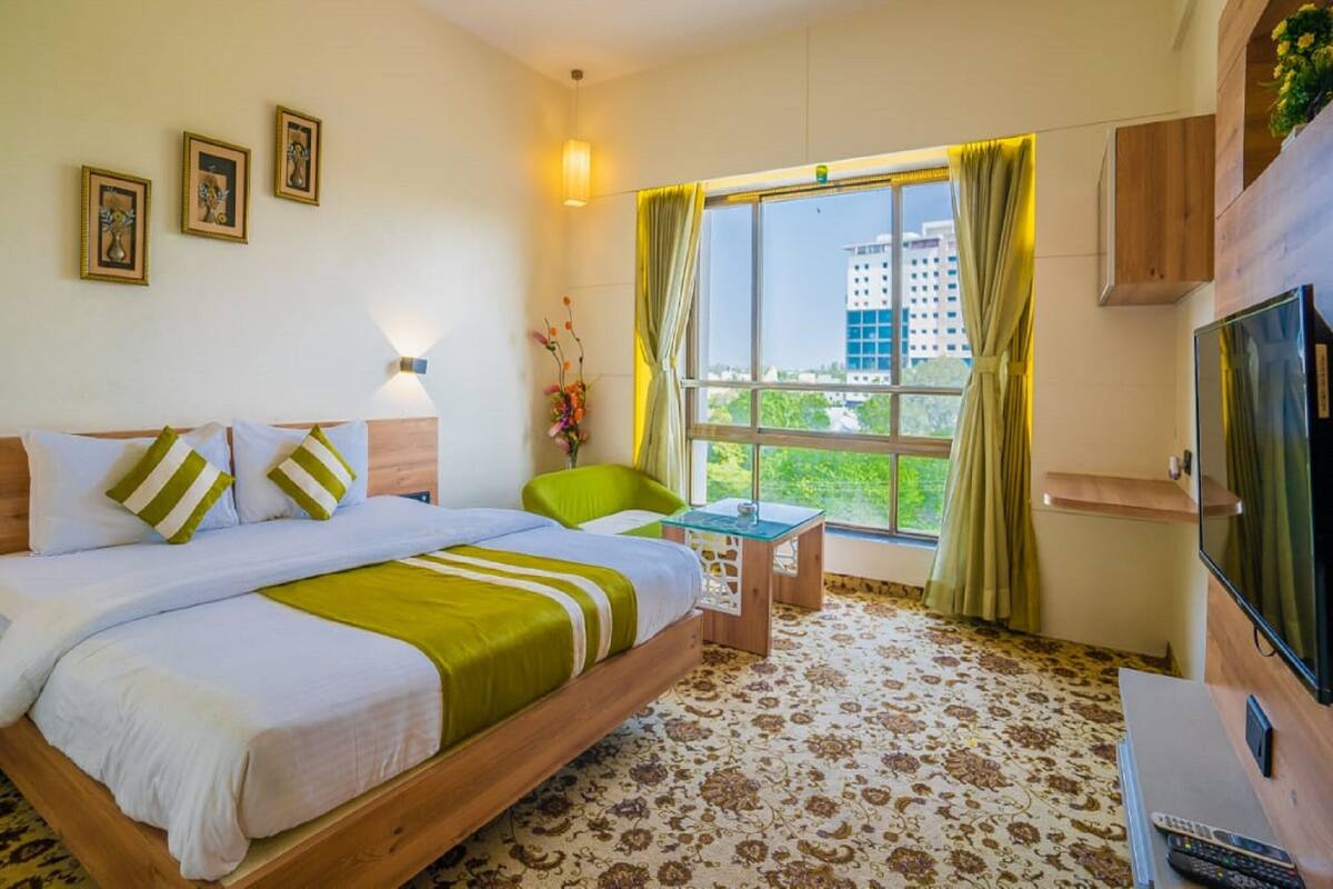 A hotel room with a bed, a small table, a TV, and a window with curtains.