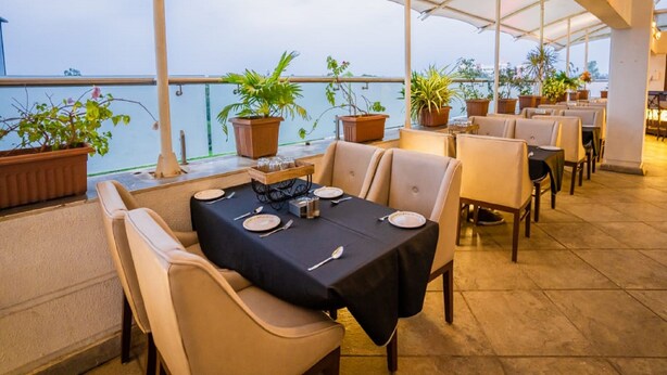 An outdoor restaurant with tables set for dining, potted plants, and a view of the water.
