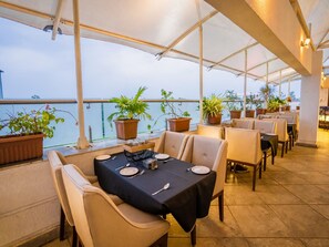 An outdoor restaurant with tables set for dining, potted plants, and a view of the water. - Hotel V Star (Ahmednagar)