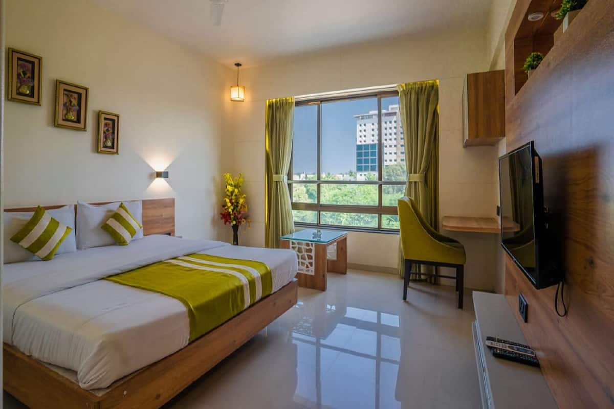 A modern hotel room with a bed, a desk, a TV, and a window with a view of buildings.