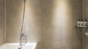 A modern bathroom with a freestanding bathtub, a handheld showerhead, and a wall-mounted shelf with toiletries. - Busan No.25 Yongho (Busan)