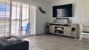 A living room with a flat-screen TV, a bookshelf, and a sliding glass door leading to a balcony.