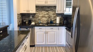 A modern kitchen with white cabinets, a black granite countertop, a stainless steel refrigerator, and a tiled backsplash.