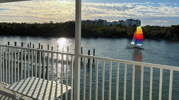 A waterfront view with a sailboat, a dock with a table, and buildings in the background.