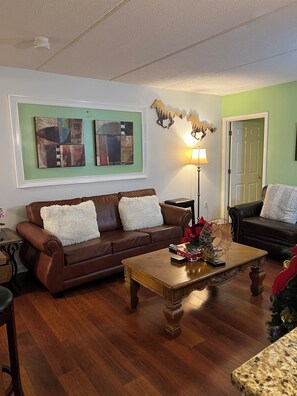 Ein Wohnzimmer mit einem braunen Ledersofa, einem Holztisch und zwei gerahmten abstrakten Bildern an der Wand.