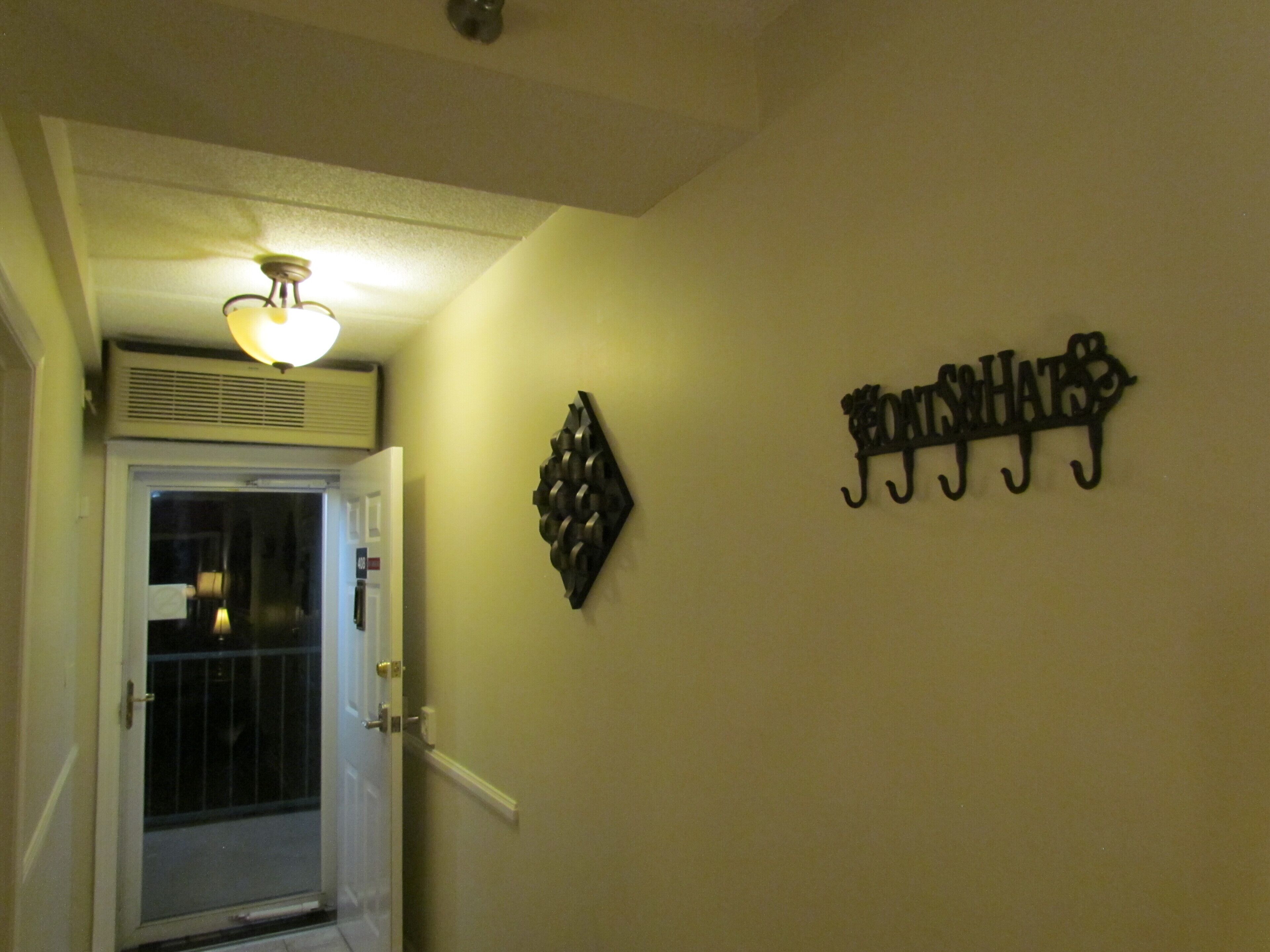 Um corredor com uma porta que dá para uma varanda, um respiradouro na parede e uma placa de metal decorativa.