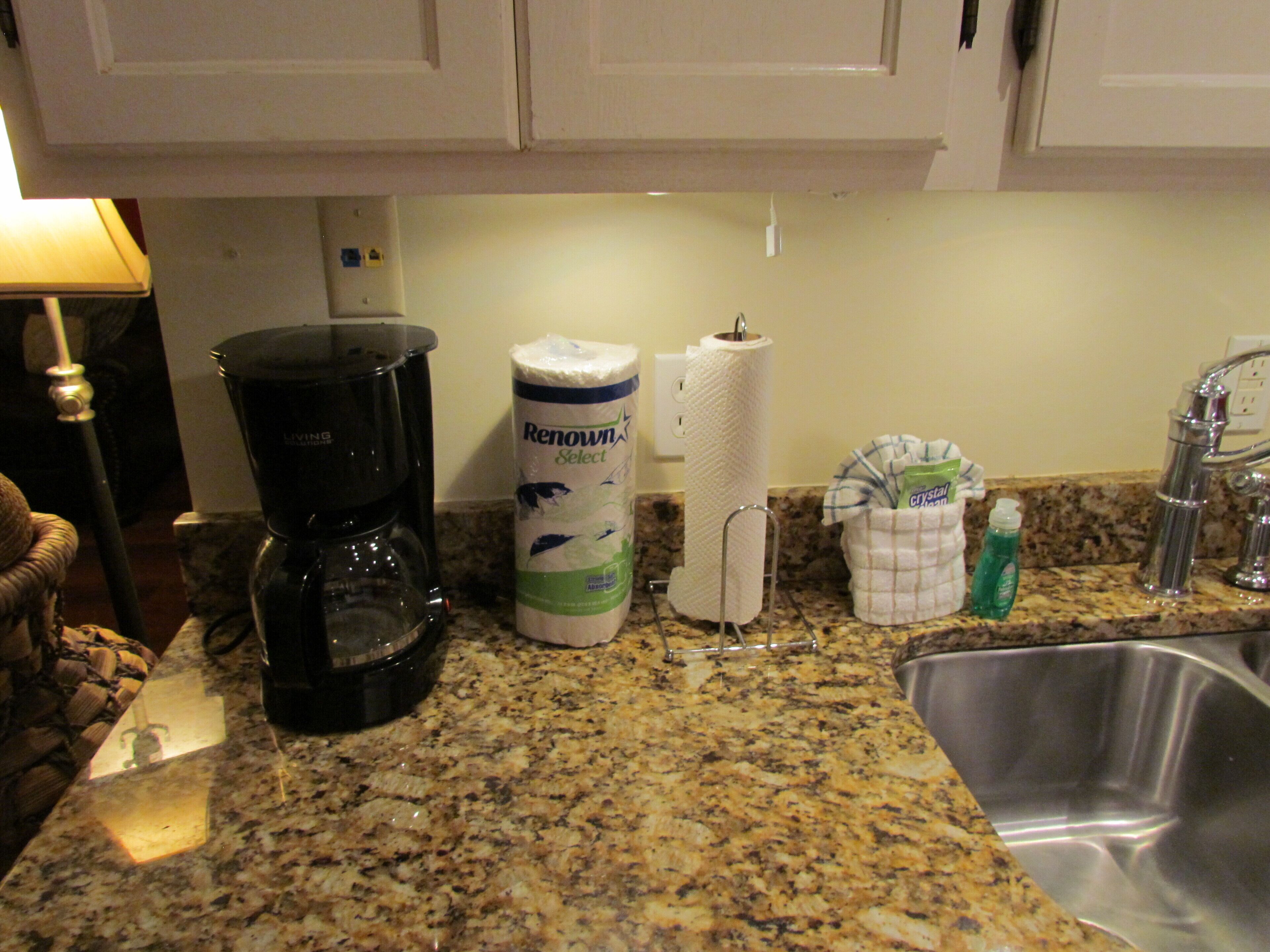 Una cocina con cafetera, dispensador de toallas de papel y un lavamanos.