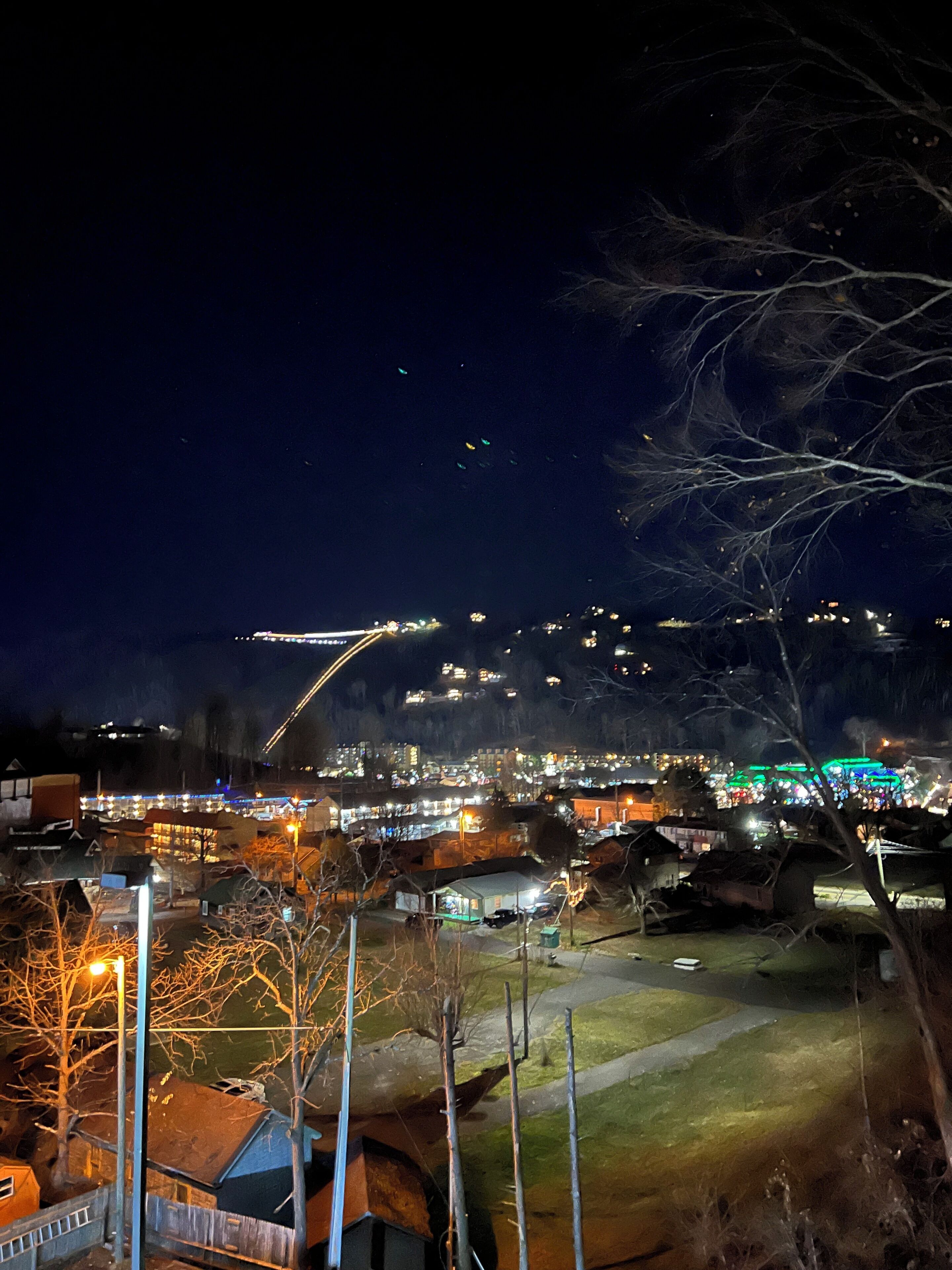 A nighttime view of a town with illuminated buildings and a bridge in the distance.