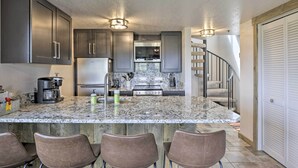 A kitchen with a marble countertop, stainless steel appliances, and a built-in island with bar stools.
