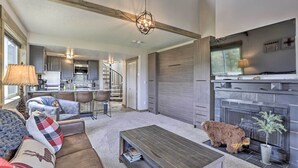 A spacious living room with a fireplace, a sofa set, and a coffee table. There is a dog sitting by the fireplace.