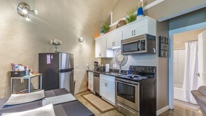 Une cuisine compacte équipée d’un réfrigérateur, d’un four à micro-ondes, d’une cuisinière et d’un évier. On y trouve une petite table avec des papiers et un panier rempli d’objets divers.