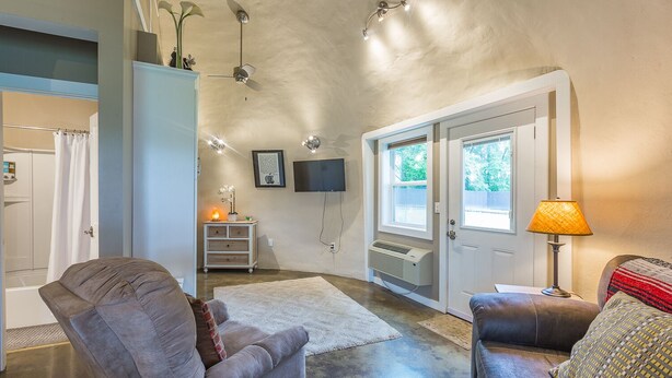 Un salon avec un canapé gris, un canapé en cuir marron, un tapis blanc, une lampe, un téléviseur et un ventilateur de plafond.