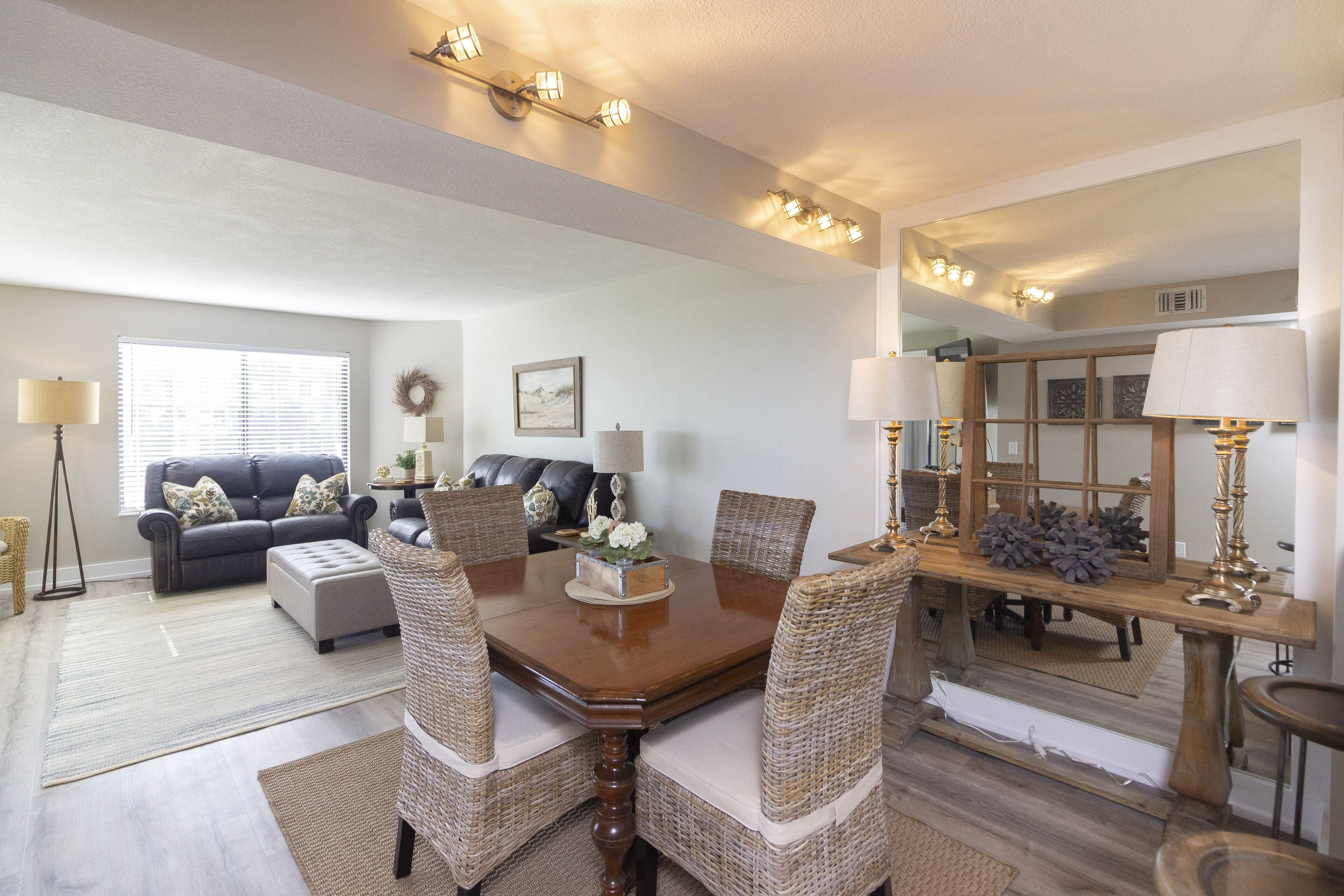 A dining area with a wooden table, wicker chairs, and a large mirror above the table.
