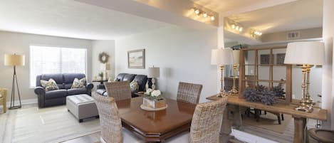 A dining area with a wooden table, wicker chairs, and a large mirror above the table.