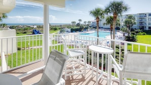 Un balcon avec des chaises et des tables blanches, donnant sur une piscine et une plage.