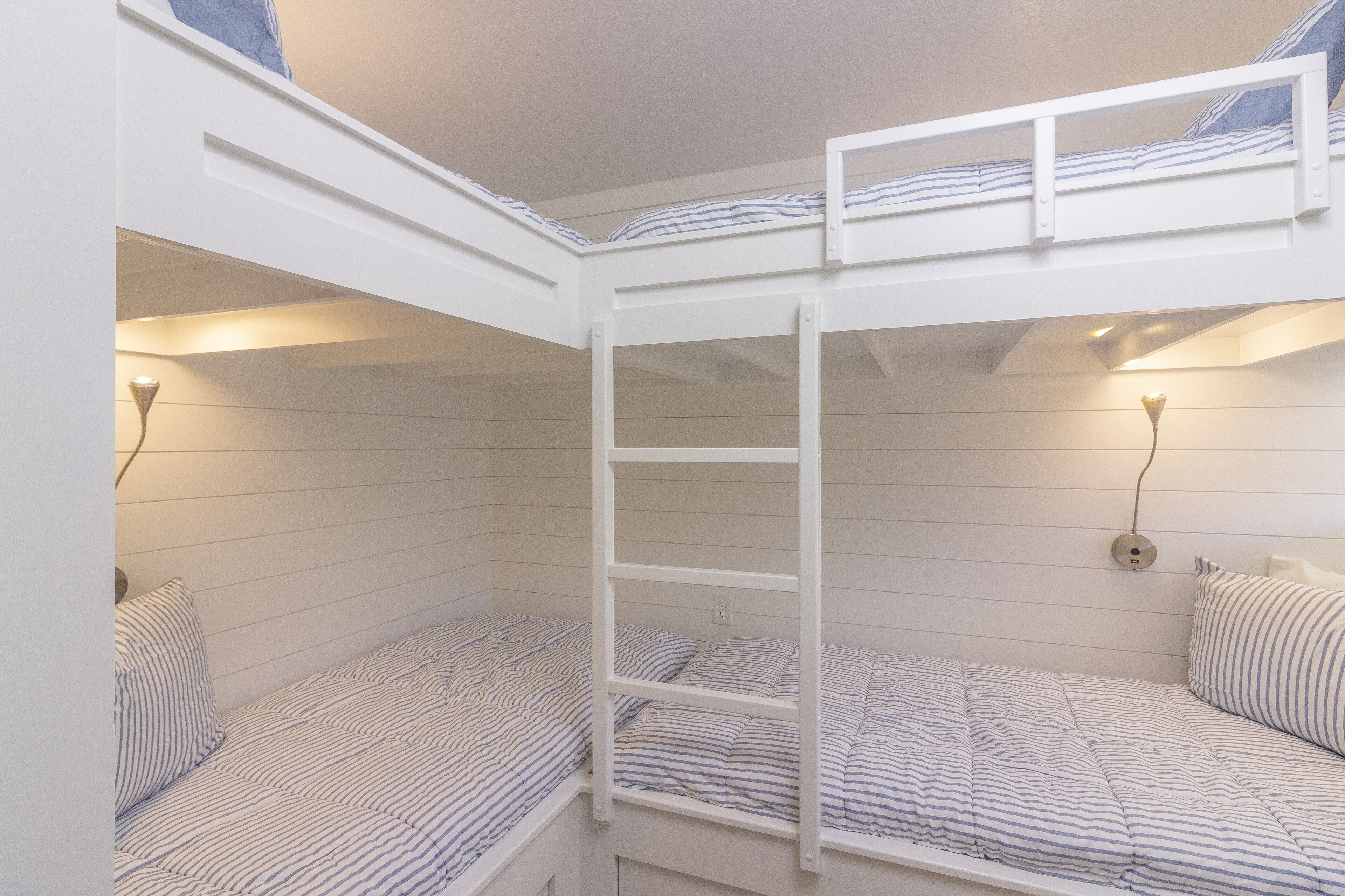 Habitación con literas, una escalera, dos camas con ropa de cama a rayas y luces fijadas en la pared.