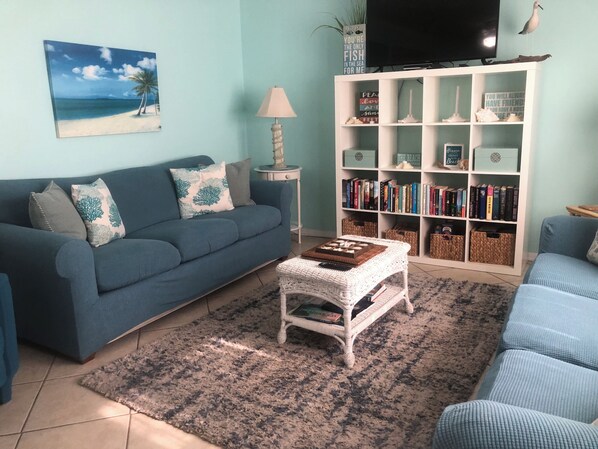 A living room with a blue sofa, a coffee table, a bookshelf, and a painting of a beach scene.