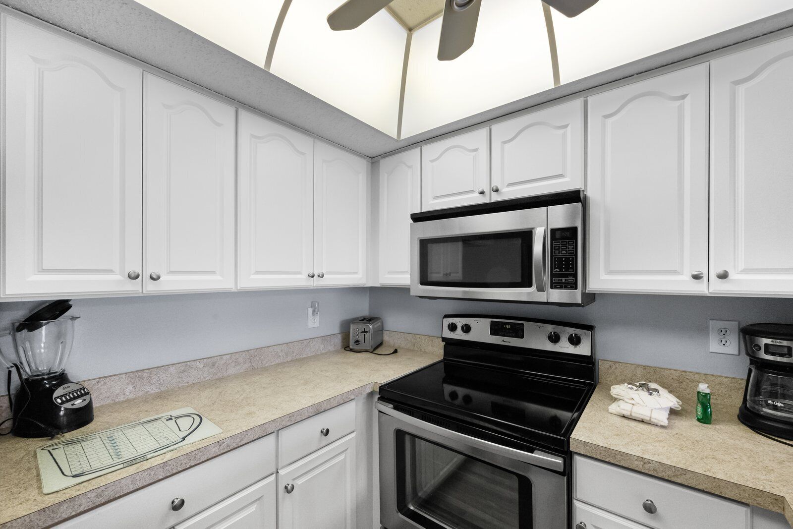 A modern kitchen with white cabinets, a built-in microwave, a stove, a toaster, and a blender.