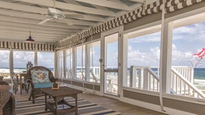 A covered outdoor area with wicker furniture, a striped rug, and a view of the beach.