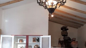 Una habitación rústica con vigas de madera a la vista, una araña, un armario rojo con estantes abiertos y un cofre de madera.