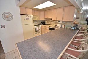 Una cocina con encimera de granito, armarios blancos, un refrigerador, un microondas y una cafetera.