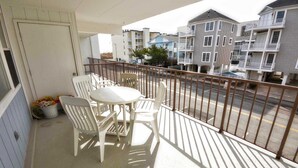 A balcony with a table and chairs, a potted plant, and a view of neighboring buildings. - Pretty, spacious 2-bedroom condo with free WiFi and adorable coastal decor located uptown and only a half a block from the beach! (Ocean City)