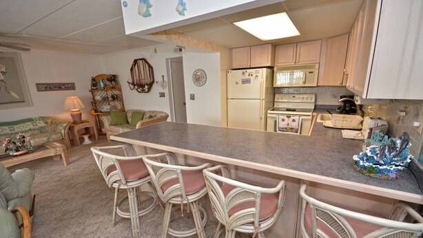 A kitchen with a central island, bar stools, a refrigerator, and a stove. - Pretty, spacious 2-bedroom condo with free WiFi and adorable coastal decor located uptown and only a half a block from the beach! (Ocean City)