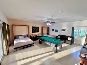 A room with a bed, a pool table, a sofa, and a ceiling fan.