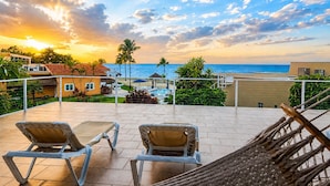 Eine Terrasse mit Liegestühlen und einer Hängematte mit Blick auf einen Strand und das Meer bei Sonnenuntergang.