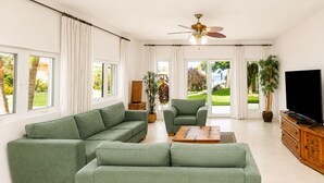 Ein modernes Wohnzimmer mit einem Ecksofa, einem Holztisch, einem Fernseher und einem Deckenventilator.