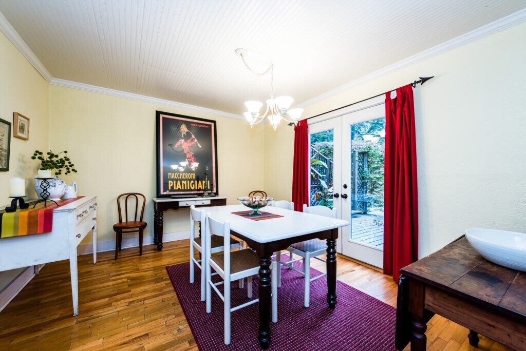 Un'area pranzo con tavolo bianco, sedie e un lampadario. Si vede un poster al muro e una finestra con tende rosse.