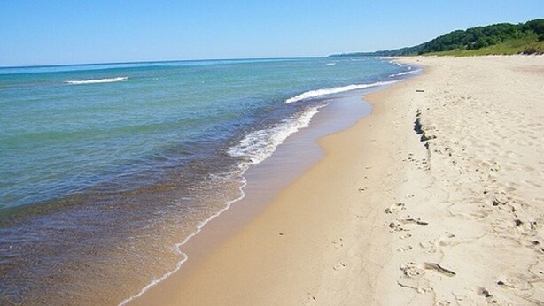 Ein sandiger Strand mit sanften Wellen und blauem Himmel.