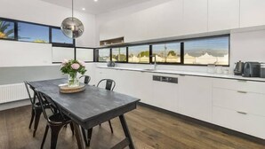 A modern kitchen with white cabinets, a dark wooden table, and a view of the countryside through large windows. - Yellow Door Coburg | Boutique Accommodation | Sleeps up to 16 guests (Coburg)