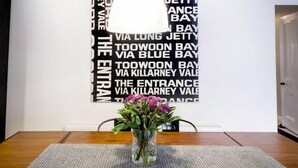 A dining table with a vase of flowers, a placemat, and a wall with a black and white text design. - Yellow Door Coburg | Boutique Accommodation | Sleeps up to 16 guests (Coburg)