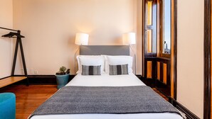 A hotel room with a bed, two bedside lamps, a small plant, and a wooden floor. - Original Studio in Bolhão Market (Oporto)