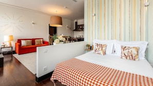 Une chambre d’hôtel avec un grand lit, un canapé rouge, un coin cuisine et un mur à rayures.