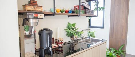 A modern kitchen with a coffee machine, shelves with decorative items, and potted plants.